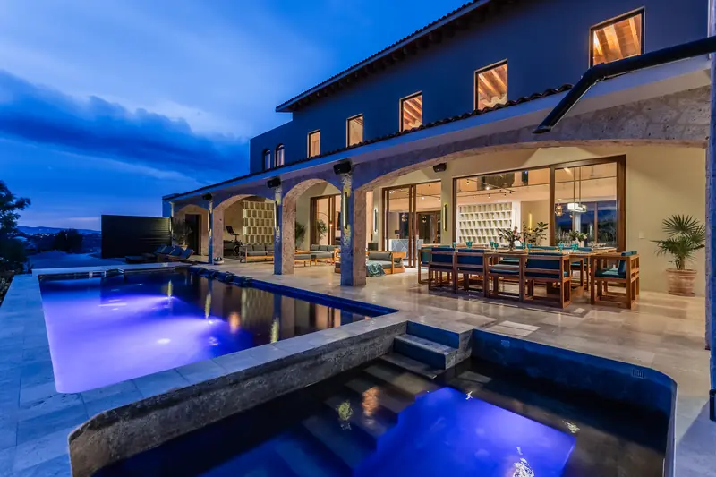 Casa de estilo hacienda al atardecer con alberca iluminada y terraza techada
