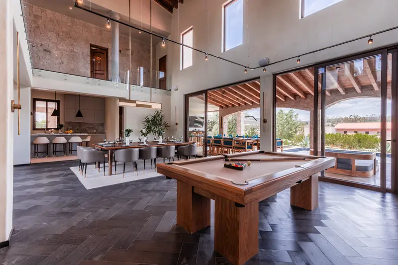 Estancia de doble altura con mesa de billar, comedor y vista al jardín